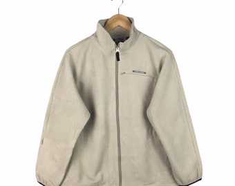 May include: A beige fleece zip-up jacket with a black zipper and a small black logo patch on the left chest. The jacket has a stand-up collar and long sleeves.