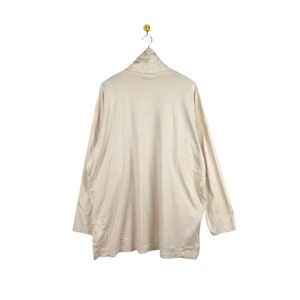 May include: A cream-colored long-sleeved shirt with a mock neck.