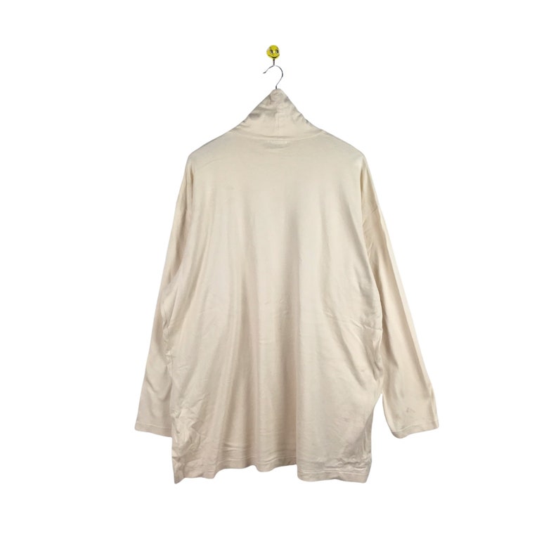 May include: A cream-colored long-sleeved shirt with a mock neck.
