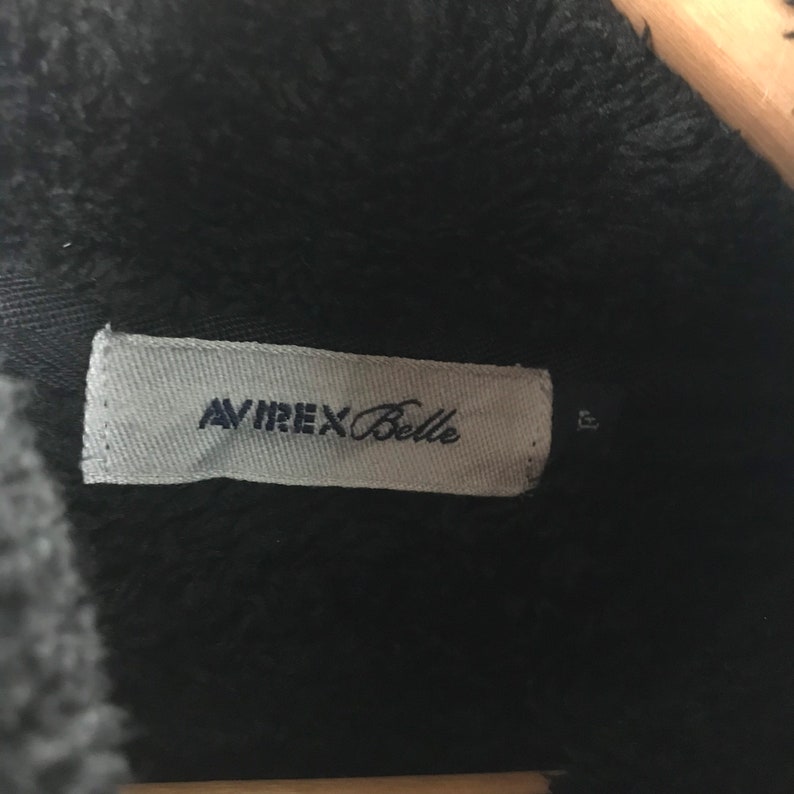 May include: A white tag with black text that reads "AVIREX Belle" on a black fuzzy jacket.