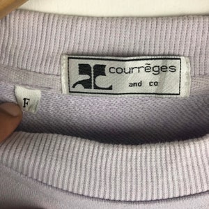 Pu&ograve; includere: Una felpa di colore lilla chiaro con un'etichetta bianca su cui &egrave; scritto "Courr&egrave;ges and co" in lettere nere. L'etichetta ha un logo "C" stilizzato in nero. La felpa ha un'etichetta di taglia che indica "F" in lettere nere.