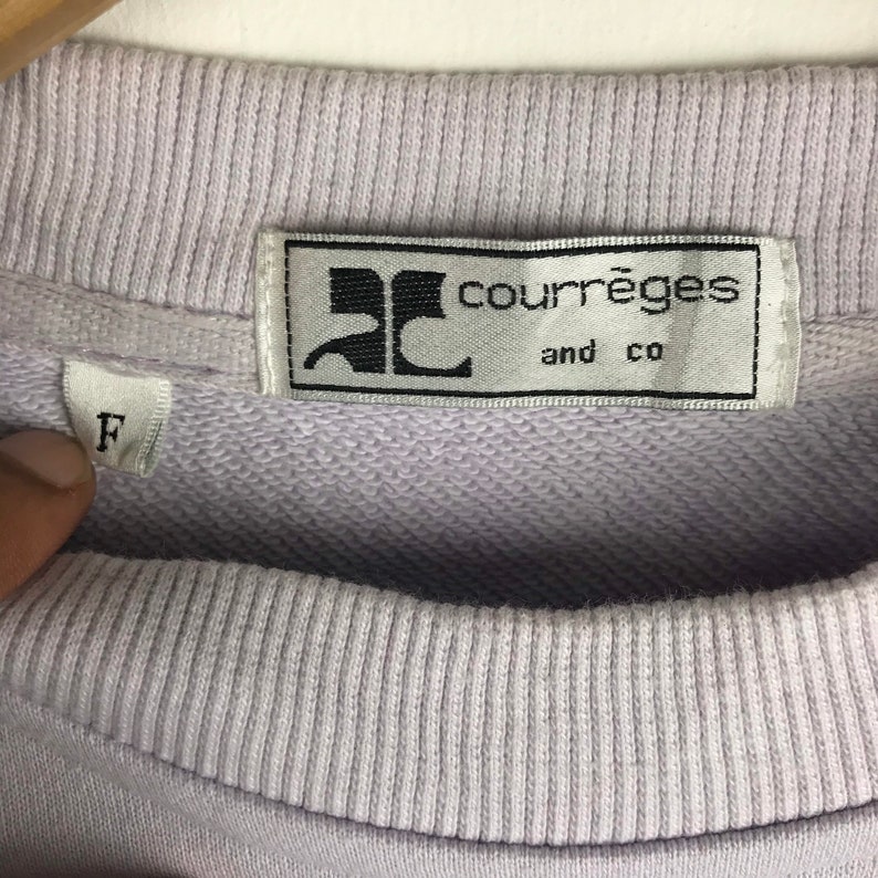 Pu&ograve; includere: Una felpa di colore lilla chiaro con un'etichetta bianca su cui &egrave; scritto "Courr&egrave;ges and co" in lettere nere. L'etichetta ha un logo "C" stilizzato in nero. La felpa ha un'etichetta di taglia che indica "F" in lettere nere.
