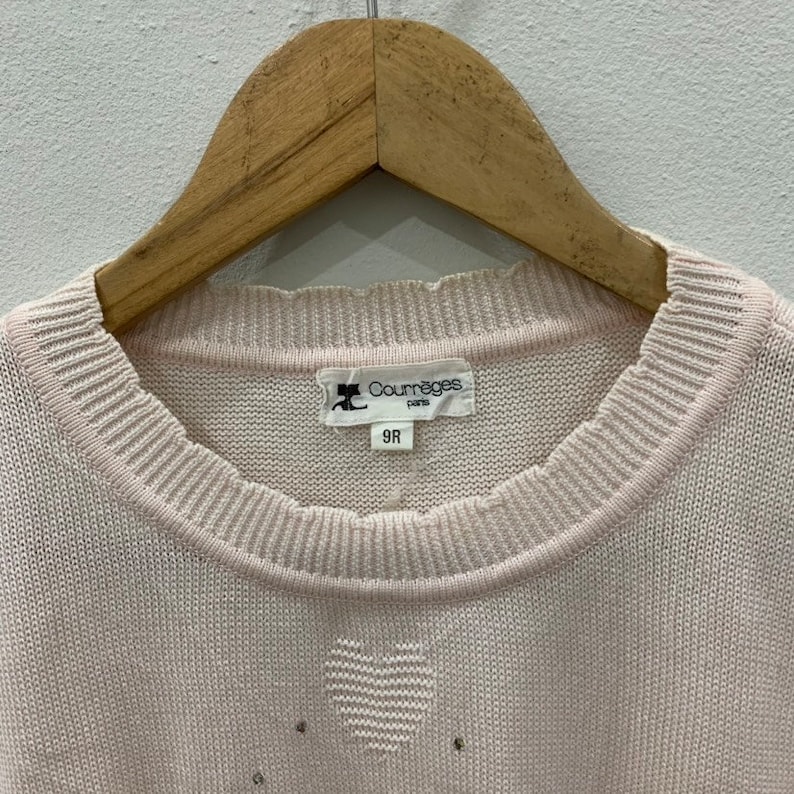 May include: A pale pink knitted sweater with a heart design and a Courr&egrave;ges Paris label. The label has the size 9R printed on it.