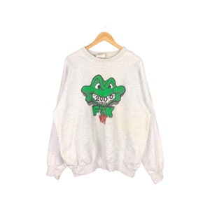 May include: A gray sweatshirt with a green cartoon frog wearing braces. The frog's mouth has the numbers 2000, 1999, 1998, and 1997 on it. The text "F2K" is below the frog.