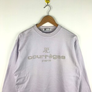 Pu&ograve; includere: Una felpa di colore lavanda con un logo ricamato bianco che recita "Courr&egrave;ges Paris".