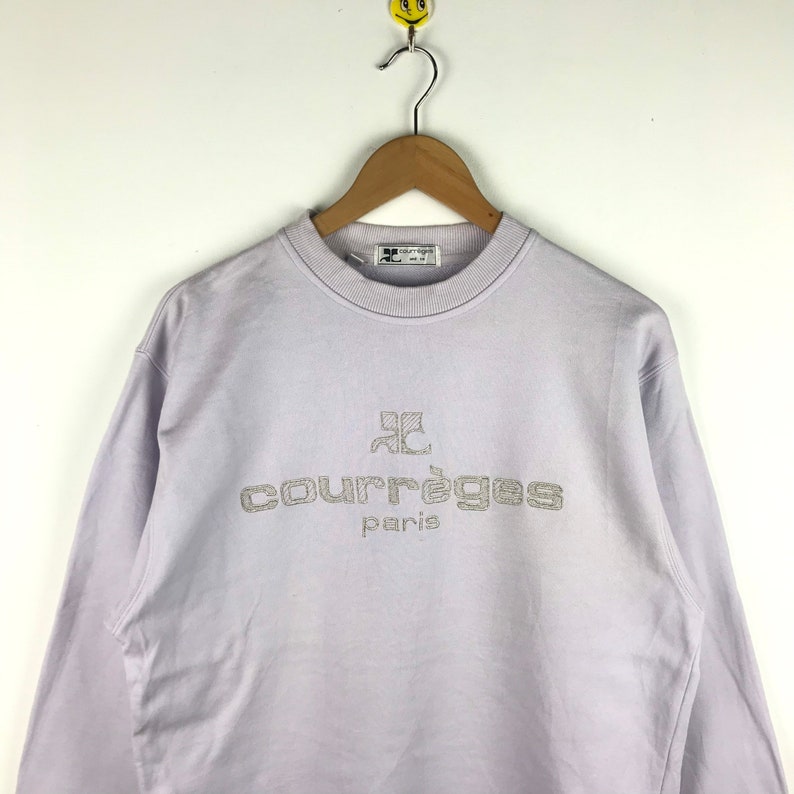 Pu&ograve; includere: Una felpa di colore lavanda con un logo ricamato bianco che recita "Courr&egrave;ges Paris".