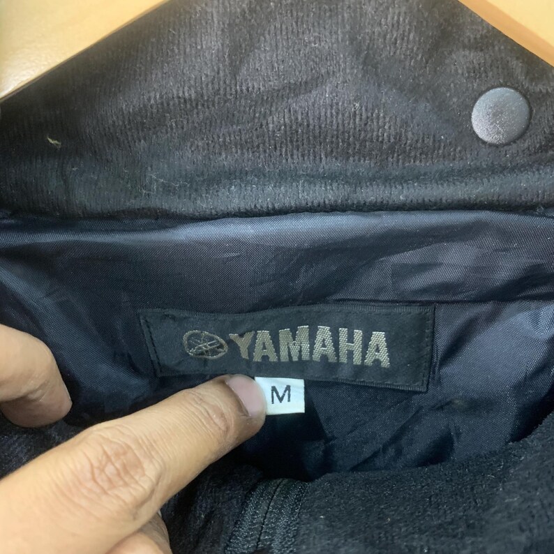 May include: Black Yamaha jacket with a size M label. The jacket has a zipper closure and a corduroy collar.