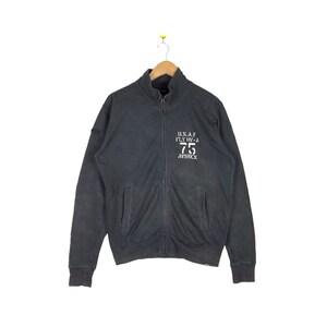 May include: A black zippered sweatshirt with a white embroidered logo that reads "U.S.A.F. FLY IN-A 75 AVIREX".