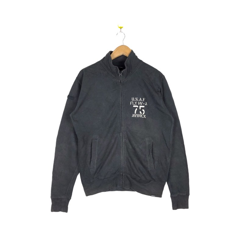 May include: A black zippered sweatshirt with a white embroidered logo that reads "U.S.A.F. FLY IN-A 75 AVIREX".