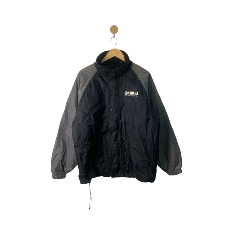 May include: A black and gray jacket with a zipper closure and a Yamaha logo on the front. The jacket has a hood and is made of a water-resistant material.