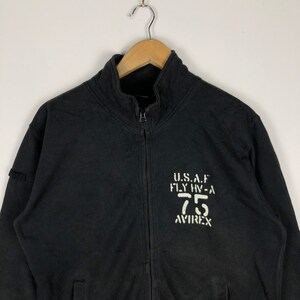 May include: Black zip-up sweatshirt with a white graphic print that reads "U.S.A.F. FLY HV-A 75 AVIREX".