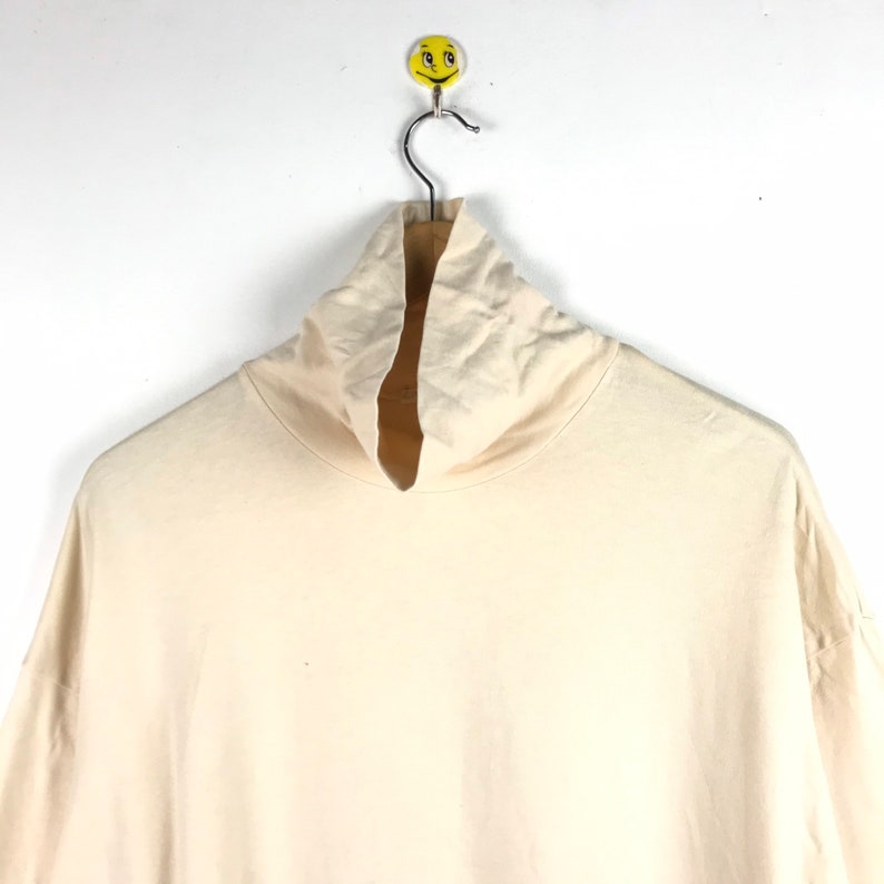 May include: A cream colored turtleneck shirt with long sleeves hanging on a hanger.