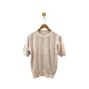 May include: A pale pink short-sleeved sweater with a delicate knit pattern and a subtle sheen. The sweater has a round neckline and a relaxed fit.