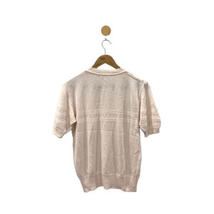 May include: A pale pink short-sleeved knitted sweater with a delicate pattern around the neckline and a horizontal band of the same pattern across the chest.