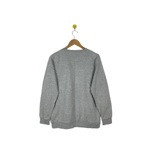 Puede incluir: Una sudadera gris con mangas largas y cuello redondo.