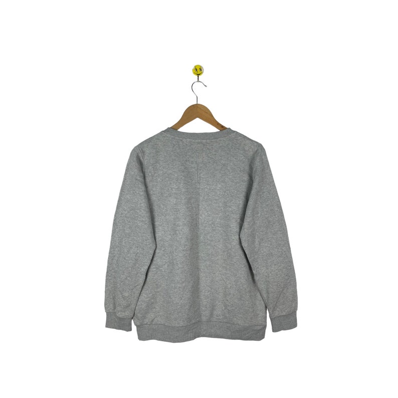 Puede incluir: Una sudadera gris con mangas largas y cuello redondo.