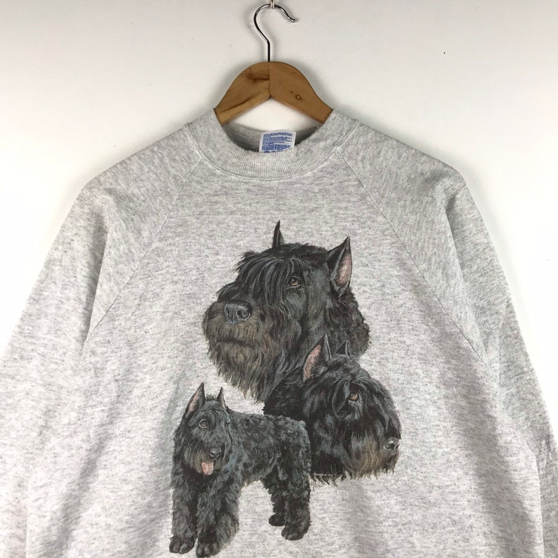 May include: A gray sweatshirt with a black and white graphic print of three Bouvier des Flandres dogs. The dogs are in different poses, with one dog's head facing the viewer, another dog's head facing to the right, and the third dog standing with its head facing to the left.