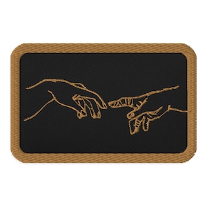 Könnte beinhalten: Ein schwarzer gestickter Patch mit einer goldenen Umrandung von zwei sich gegenseitig erreichenden Händen, inspiriert von Michelangelos Die Erschaffung Adams.