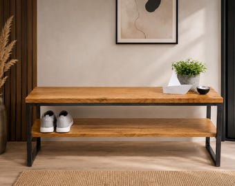 May include: A rectangular wooden bench with a natural grain finish and a black metal frame. The bench features two horizontal tiers for storage, with a pair of grey trainers placed on the lower shelf. The design is open and functional.