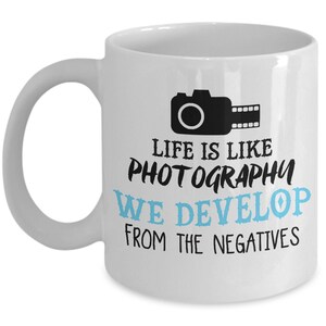 May include: White ceramic coffee mug with a black camera and film strip graphic. The text reads "Life is like photography we develop from the negatives".