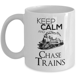 May include: White ceramic mug with black text that reads "Keep Calm and Chase Trains". A black and white illustration of a steam engine is in the center of the mug.