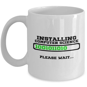 May include: White ceramic coffee mug with a black and green design that says "Installing Computer Science 1001011010 Please Wait..."