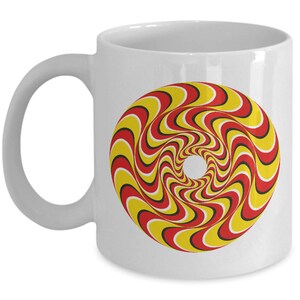 May include: White ceramic coffee mug with a red, yellow, and black optical illusion design. The design is a swirling pattern that creates a sense of movement.