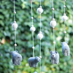 K&ouml;nnte beinhalten: Ein wei&szlig;es Holz-Babymobil mit grauen Filztier-Spielzeugen, die daran h&auml;ngen. Das Mobile hat wei&szlig;e Pompons und Holzperlen an den Schn&uuml;ren.