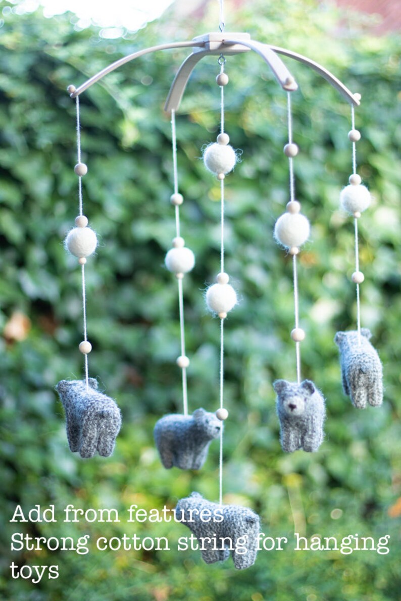 K&ouml;nnte beinhalten: Ein wei&szlig;es Holz-Babymobil mit grauen Filztier-Spielzeugen, die daran h&auml;ngen. Das Mobile hat wei&szlig;e Pompons und Holzperlen an den Schn&uuml;ren.