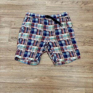 May include: Multi-colored plaid shorts with a black belt. The shorts feature a classic plaid pattern in shades of blue, red, white, and green. The shorts are made of a lightweight fabric, perfect for warm weather.
