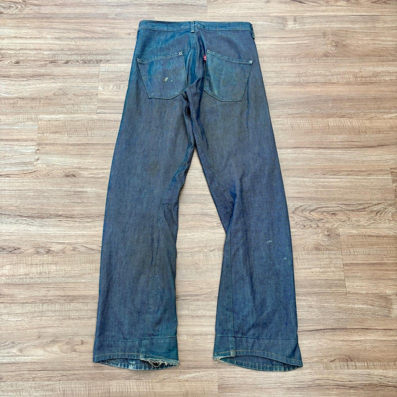 May include: Dark blue denim jeans with a wide leg design. The jeans have two back pockets and a red Levi's tag. The jeans are laid flat on a wooden surface.