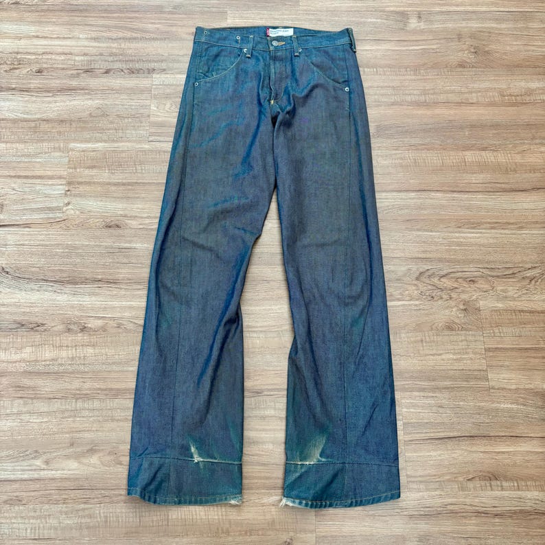 May include: Blue denim jeans with a button and zip fastening. The jeans feature a classic five-pocket design and a straight leg fit. The denim has a faded look with distressed details near the hem.