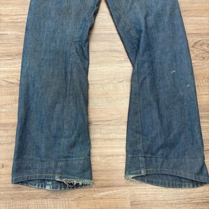 May include: Light blue denim jeans with a wide leg. The jeans feature a classic five-pocket design and a button and zip closure. The hemline is frayed, giving them a vintage appearance.