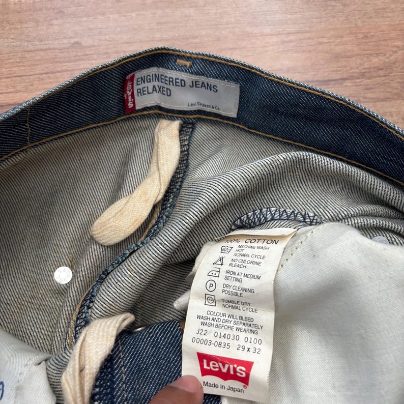 May include: Close-up of blue denim Levi's Engineered Jeans Relaxed. The jeans have a white tag with washing instructions and the Levi's logo. The tag also indicates the size is 29 x 32.