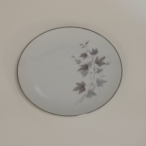 May include: A white ceramic plate with a silver rim. The plate features a delicate design of gray and purple leaves and stems. This elegant plate is suitable for serving meals.