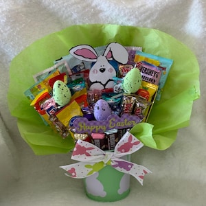 May include: An Easter-themed candy bouquet featuring a white bunny cutout, speckled eggs, and a "Happy Easter" sign. The bouquet is wrapped in green tissue paper and tied with a bow. Assorted candy bars and treats are visible.