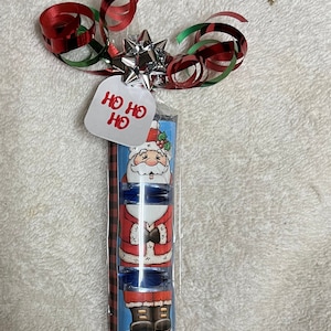 May include: A wrapped gift with a Santa Claus design and a red and green plaid pattern. The gift is tied with a red and green ribbon and a silver star. The gift tag says "Ho Ho Ho".