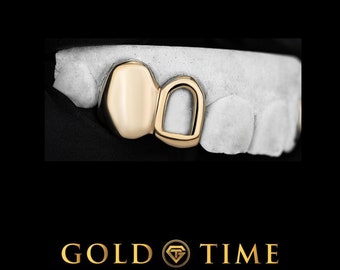 Könnte beinhalten: Goldzahn-Grill mit zwei Zähnen, einer rund und einer mit einem Loch in der Mitte. Der Grill ist aus Gold und auf einem weißen Abdruck befestigt.