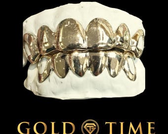 Puede incluir: Una parrilla de dientes de oro, un conjunto de dientes de oro, en un molde blanco. La parrilla está hecha de oro y tiene un acabado brillante. La parrilla es un accesorio popular de la cultura hip hop.
