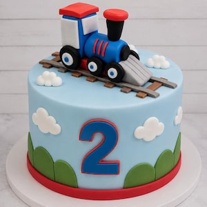May include: A cylindrical cake with light blue frosting, decorated with a red number 2, green hills, and white clouds. A blue, red, and white toy train engine sits on top of brown train tracks, completing the scene on this celebratory dessert.