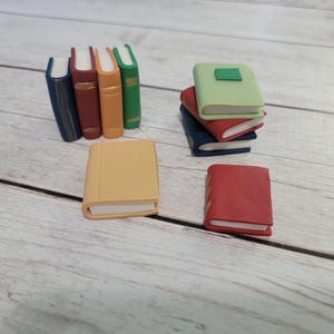 May include: A collection of miniature books in various colors, including blue, red, green, and tan. Some books are stacked, while others stand upright. The books are arranged on a light-colored wooden surface.