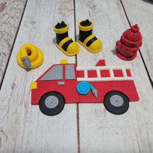 May include: A set of red, white, and yellow fondant cake toppers featuring a fire truck, two boots, a fire hydrant, and a hose.