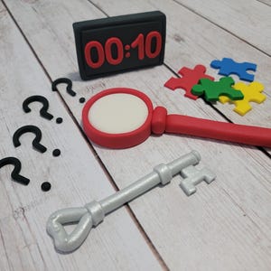 May include: A black digital timer with the time 00:10, a red magnifying glass, a silver key, and four colorful puzzle pieces on a wooden surface.
