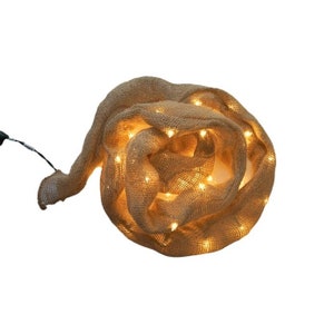 May include: A string of warm white LED lights wrapped in burlap fabric. The lights are coiled together in a circular shape.