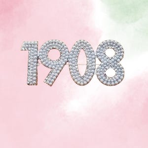 May include: A silver-toned brooch shaped like the number 1908, made of small white pearls.