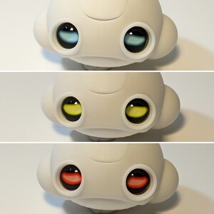 May include: A white toy with a round head and two large eyes. The eyes are blue, yellow, and red in color.