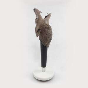Peut inclure: Une sculpture de tête de loup en brun et gris avec la gueule ouverte, montée sur un socle noir et blanc. La sculpture est faite d'un matériau texturé qui ressemble à de la fourrure.