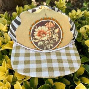 May include: A yellow and white gingham baseball cap with a brown and white floral patch on the front.