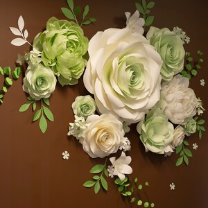 Puede incluir: Una pared decorada con flores de papel en tonos blancos y verdes. Las flores est&aacute;n dispuestas en un racimo e incluyen rosas, peon&iacute;as y otras variedades.