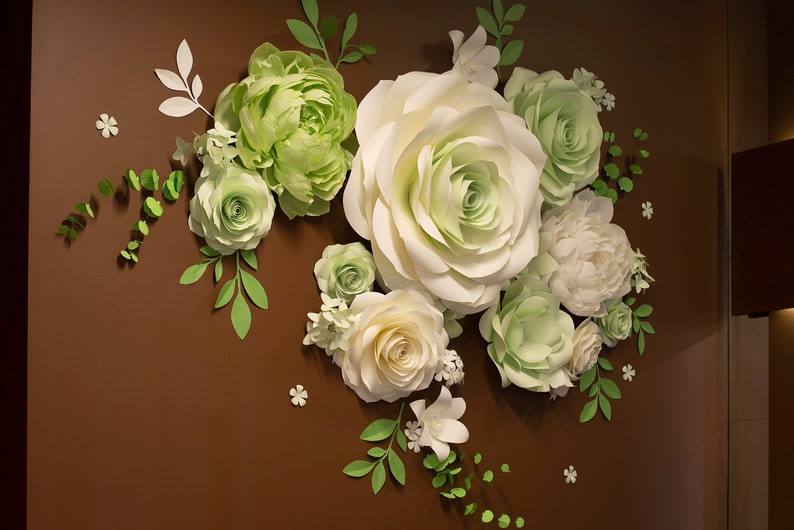 Puede incluir: Una pared decorada con flores de papel en tonos blancos y verdes. Las flores est&aacute;n dispuestas en un racimo e incluyen rosas, peon&iacute;as y otras variedades.